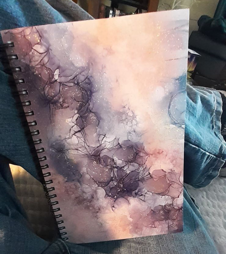 A spiral journal with misty purple, pink, and blue alcohol ink clouds.