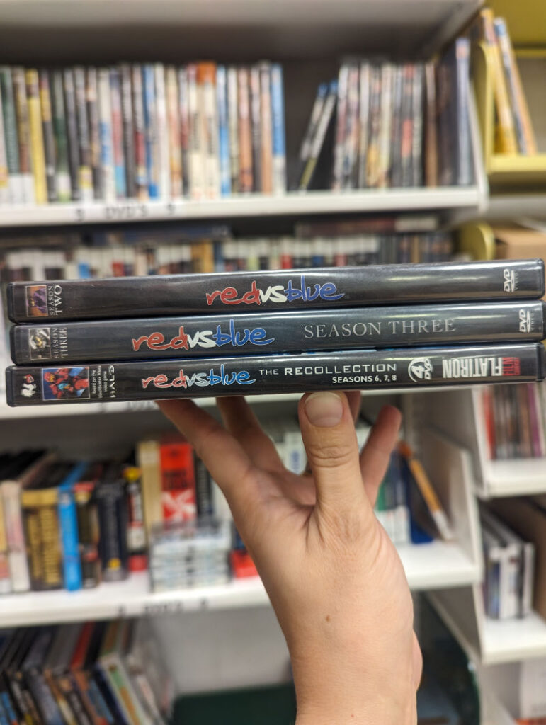 Three Red vs. Blue DVDs from Rooster Teeth, balanced on my hand like a serving plate.