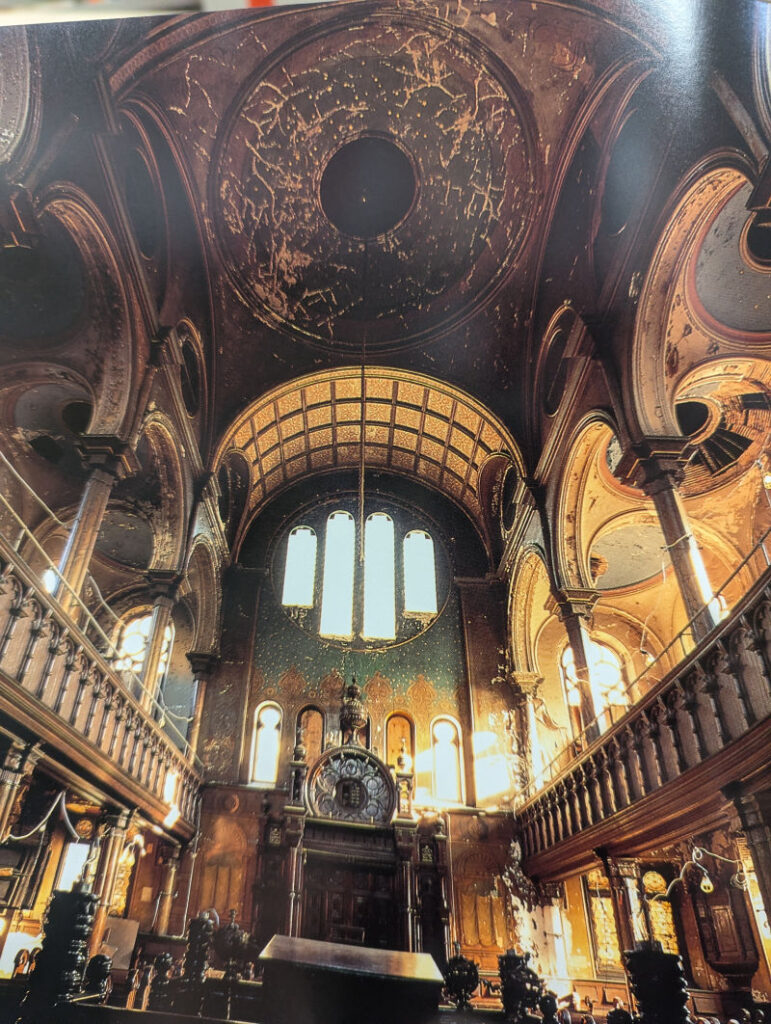 A photograph of a photograph, featuring the ruined interior of the Eldridge Street Synagogue. The dome is particularly interesting, with gold-like scratches across the dome.