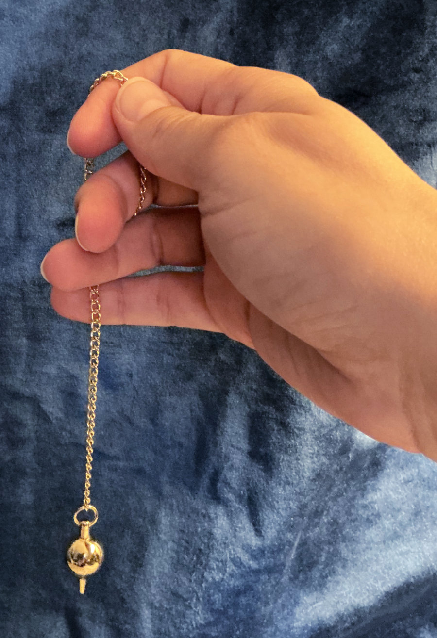 A female hand holding a golden pendulum.